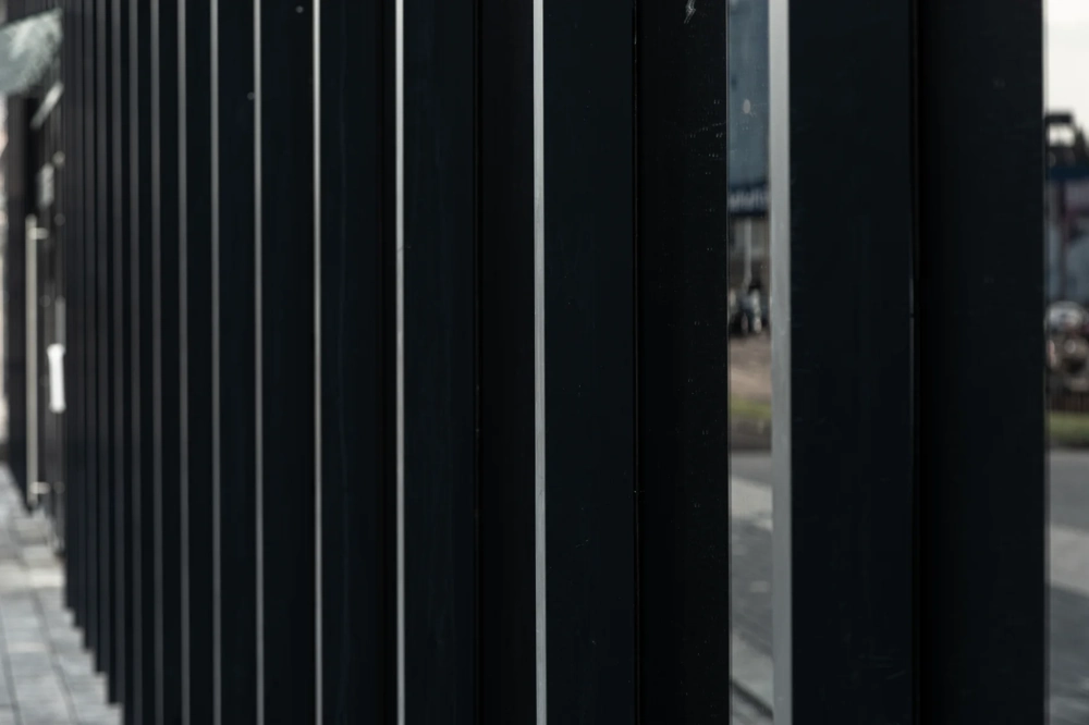 Zbliżenie czarnego metalowego ogrodzenia palisadowego z pionowymi profilami na tle drogi