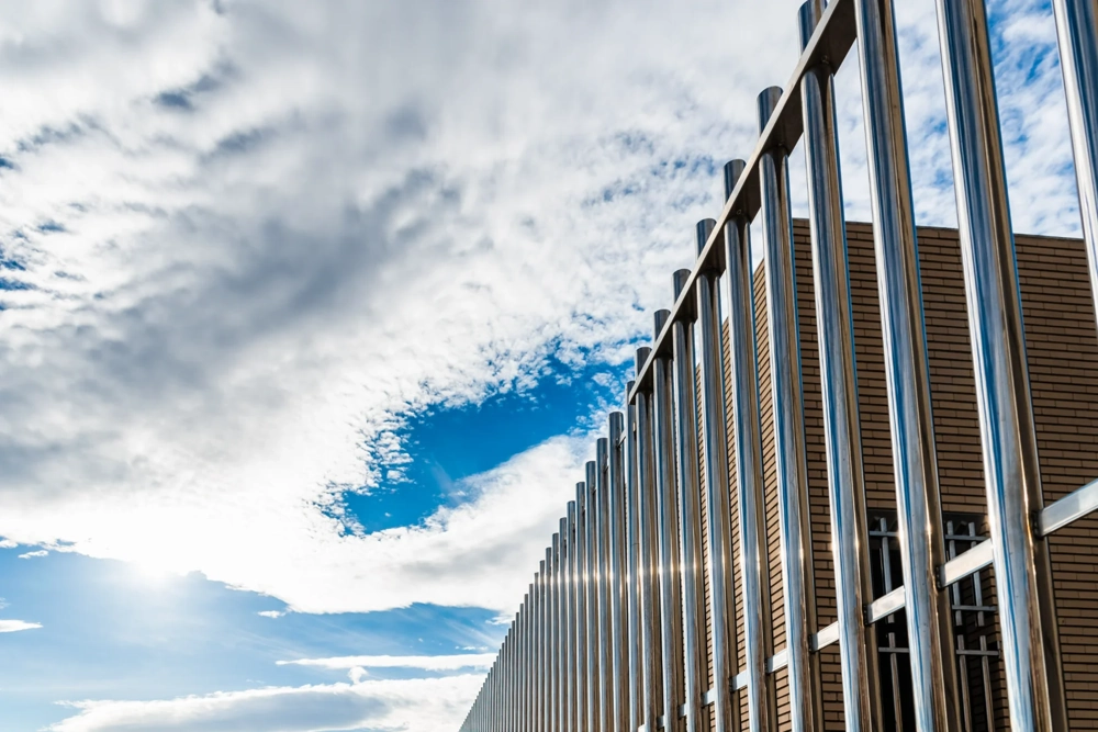 Malowanie proszkowe ogrodzenia grzebieniowego z metalowych prętów na tle nieba z chmurami