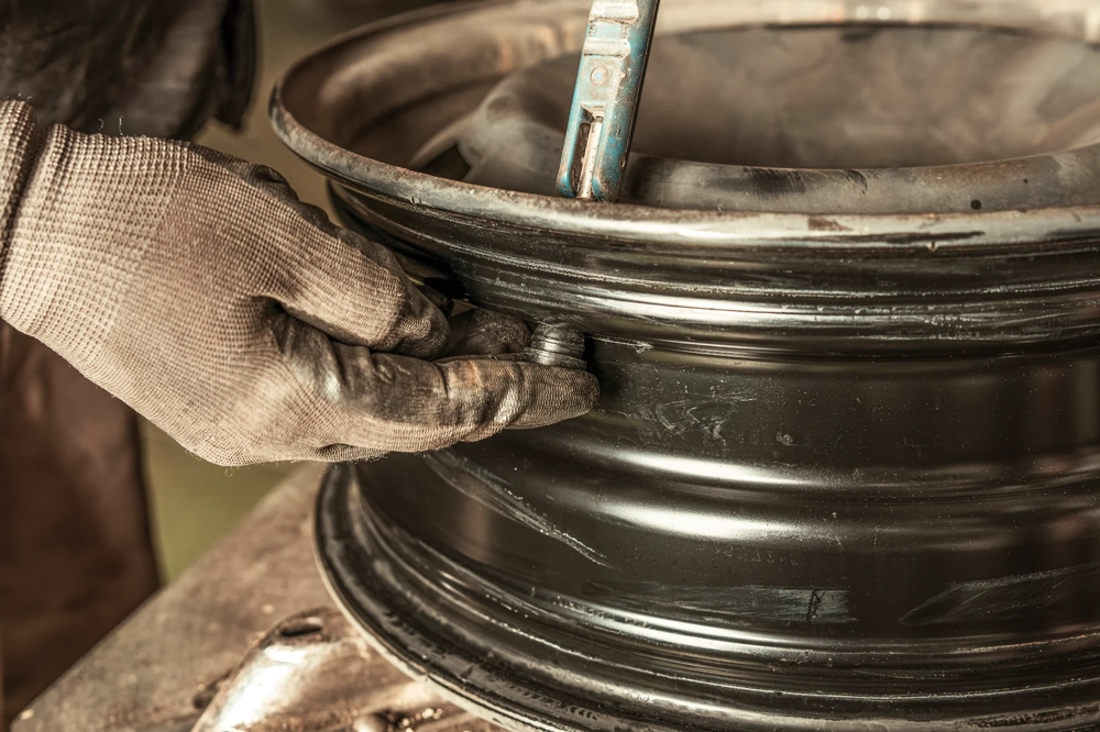 Renowacja felg: rękawicowana dłoń przygotowuje powierzchnię metalowej felgi samochodowej przed malowaniem proszkowym