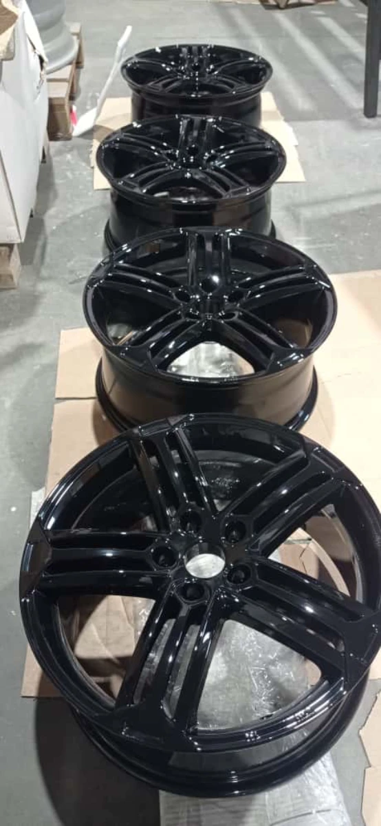 Lakierowanie proszkowe czarnych, błyszczących felg samochodowych ułożonych w rzędzie na hali warsztatowej