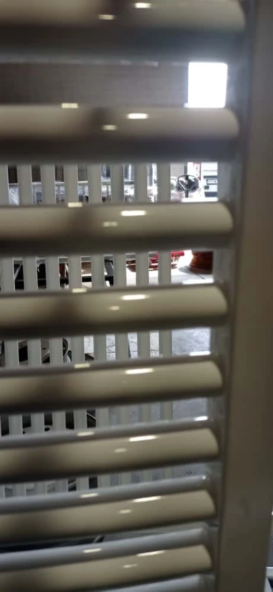 Przęsło ogrodzenia żaluzjowego z białymi poziomymi lamelami i widokiem na wózek widłowy w tle